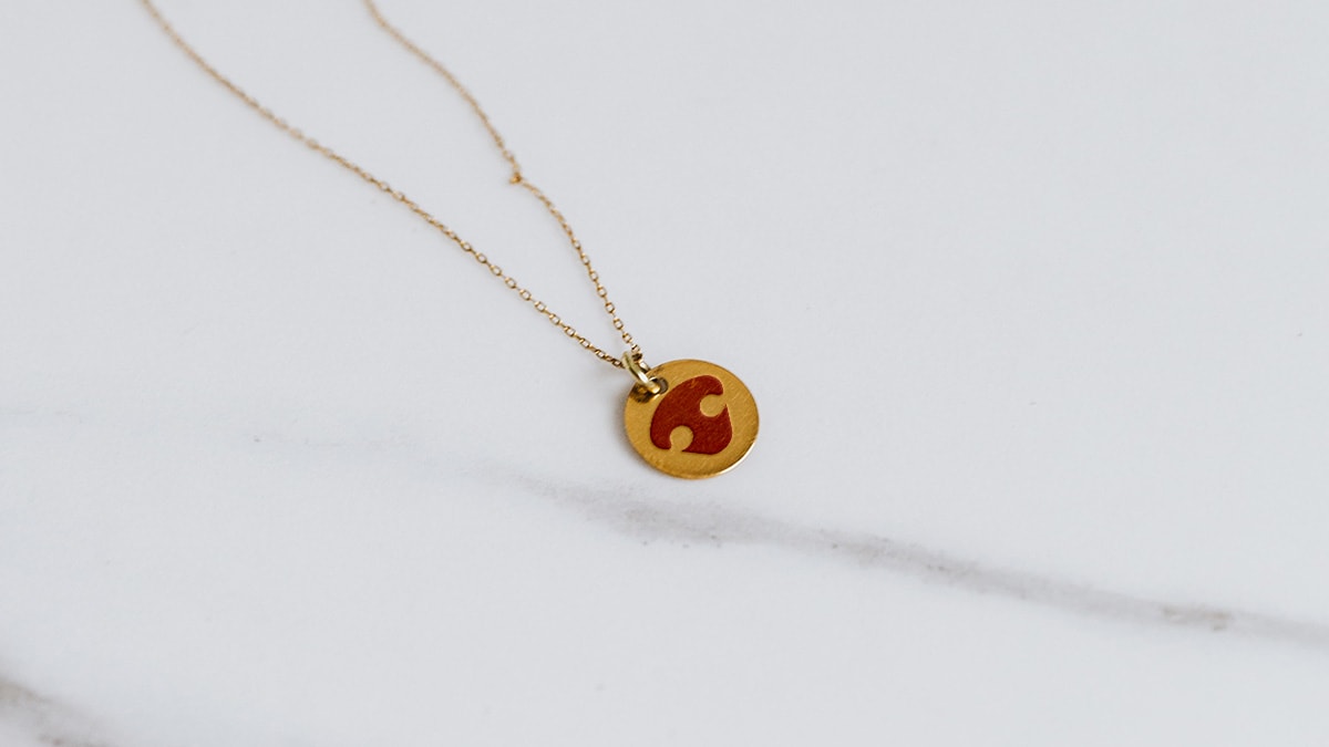 A necklace with a paw print as a pendant. It is yellow and red in color and the chain is gold.