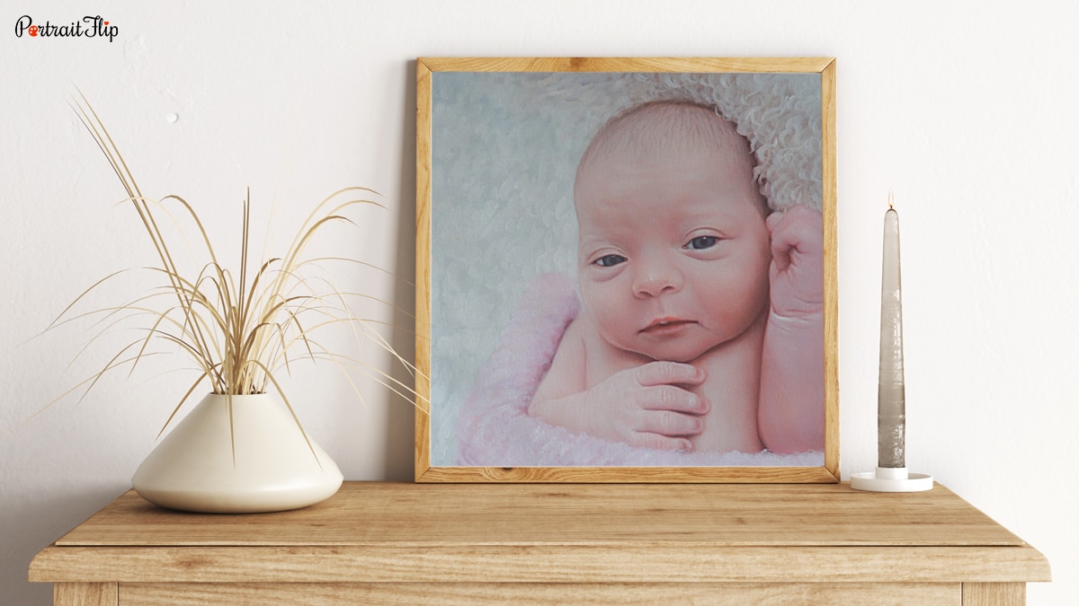 A handmade custom painting given a s a gift for the birth of a baby on a beautiful desk with decorative pieces around the portrait.