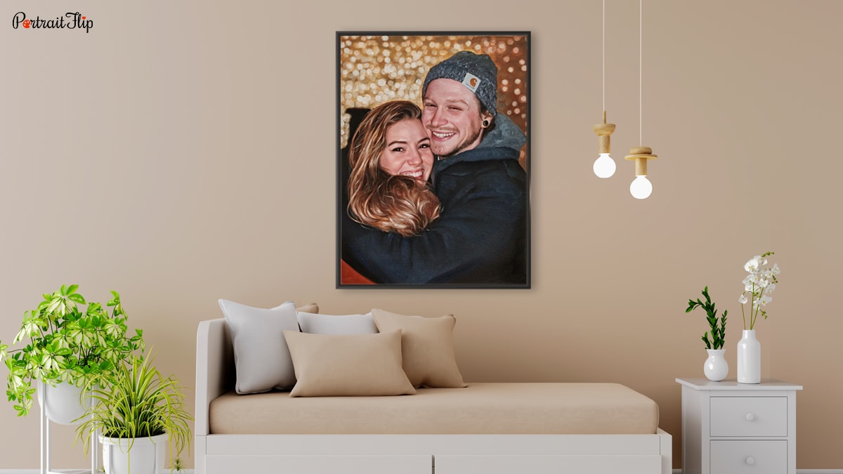 A custom handmade painting of a couple that is sitting on a wall over a couch with pretty light, a table with plants on them and some other plants as well.