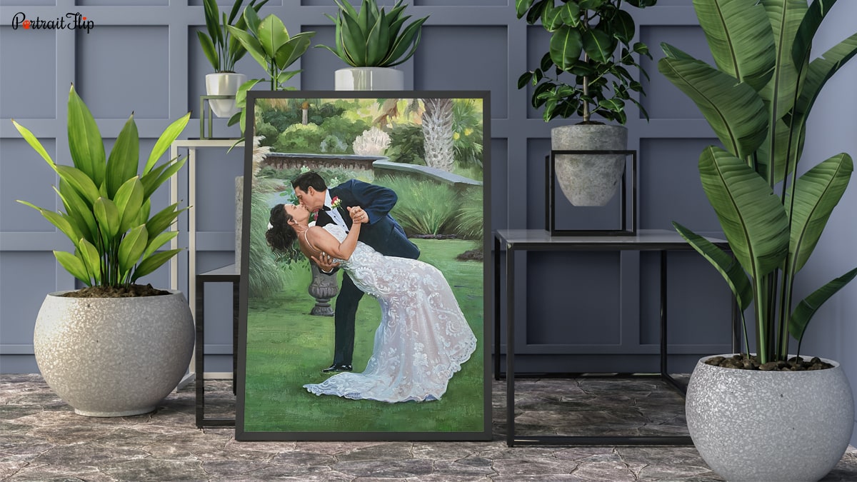 A handmade custom painting of a bride and groom kissing, the painting is placed in a very pretty interior with plants.