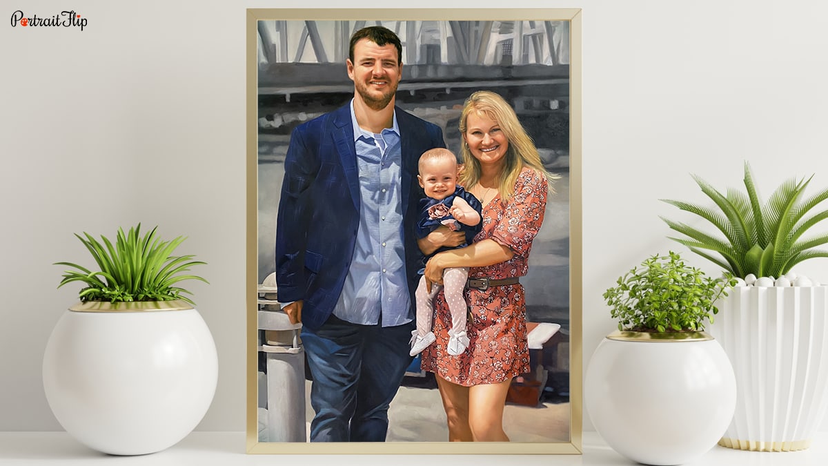 A handmade custom painting of a family, a father a mother and a baby. This painting is sitting on a table and there are plants surrounding it.