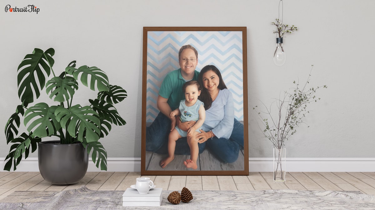 A handmade custom painting of a family of three sitting on a wooden floorboard with some plants around them.
