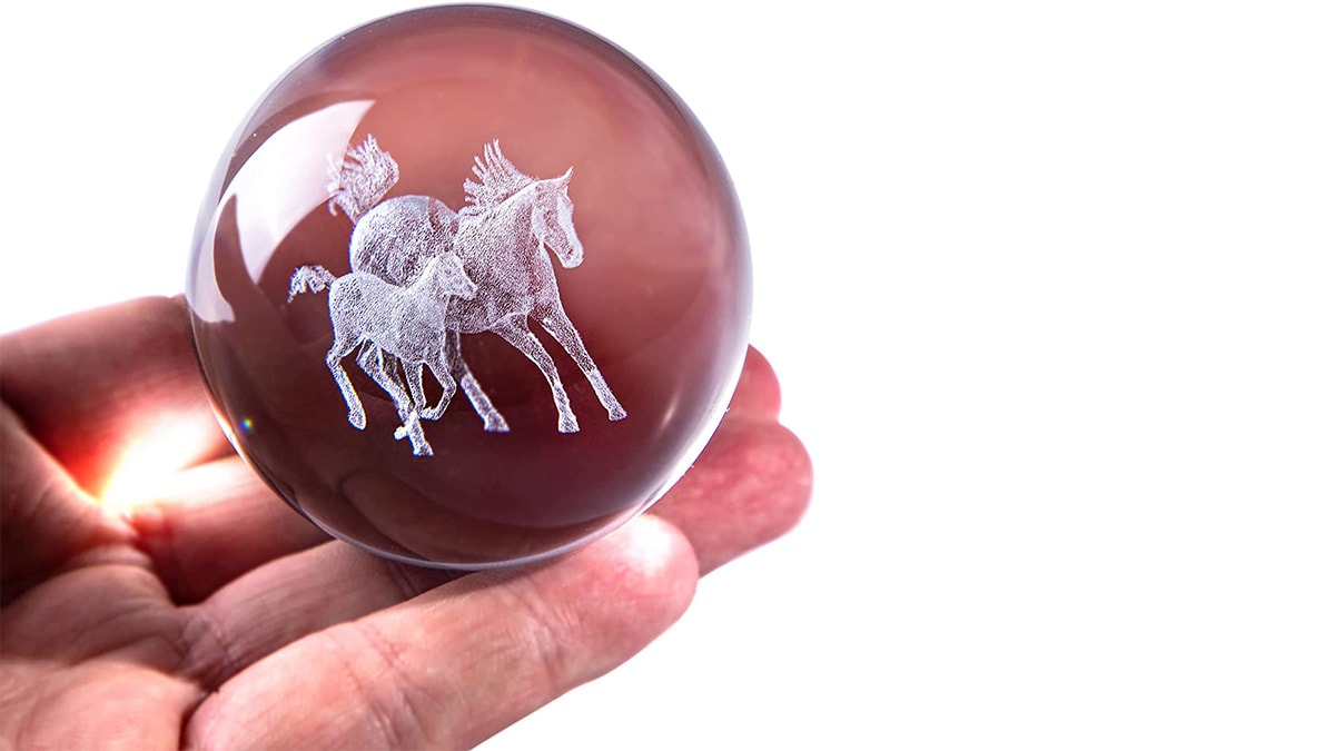 A hand holding a glass crystal with a horse in it.
