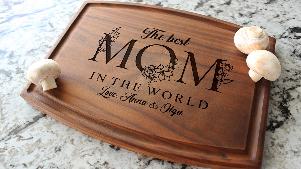 "The best Mom in the world. love, Anna and olga" is engraved on a brown cutting board. 