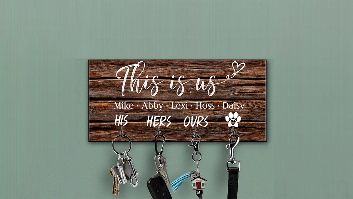 A personalized wooden key holder with their dogs name on the key holder as well. The text reads This is us and their names are written there. It is hanging on a wall.