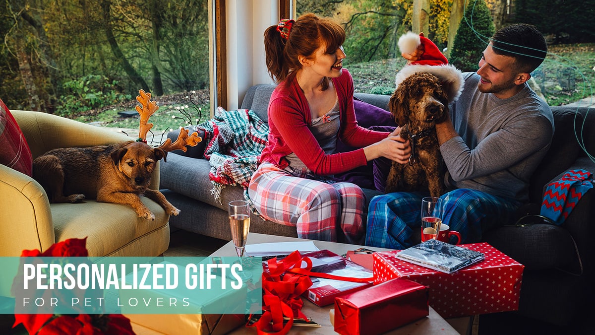 An image of a couple with two dogs sitting on a sofa with red gifts and white polka dots. the dog also has a christmas cap on and the other one has reindeer cap on. The text reads personalized gifts for pet lovers.