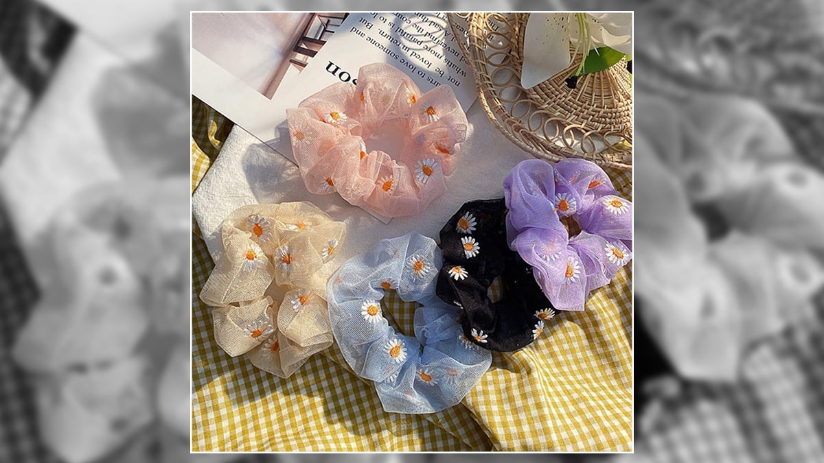 5 Scrunchies sitting on a picnic table mat with decorative pieces near them they are pink, cream, black, purple, blue in color. 