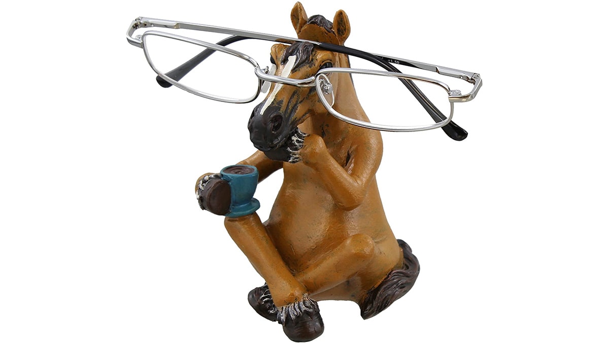 A horse spectacle stand with glasses on it and the horse is holding a cup in his hoof.
