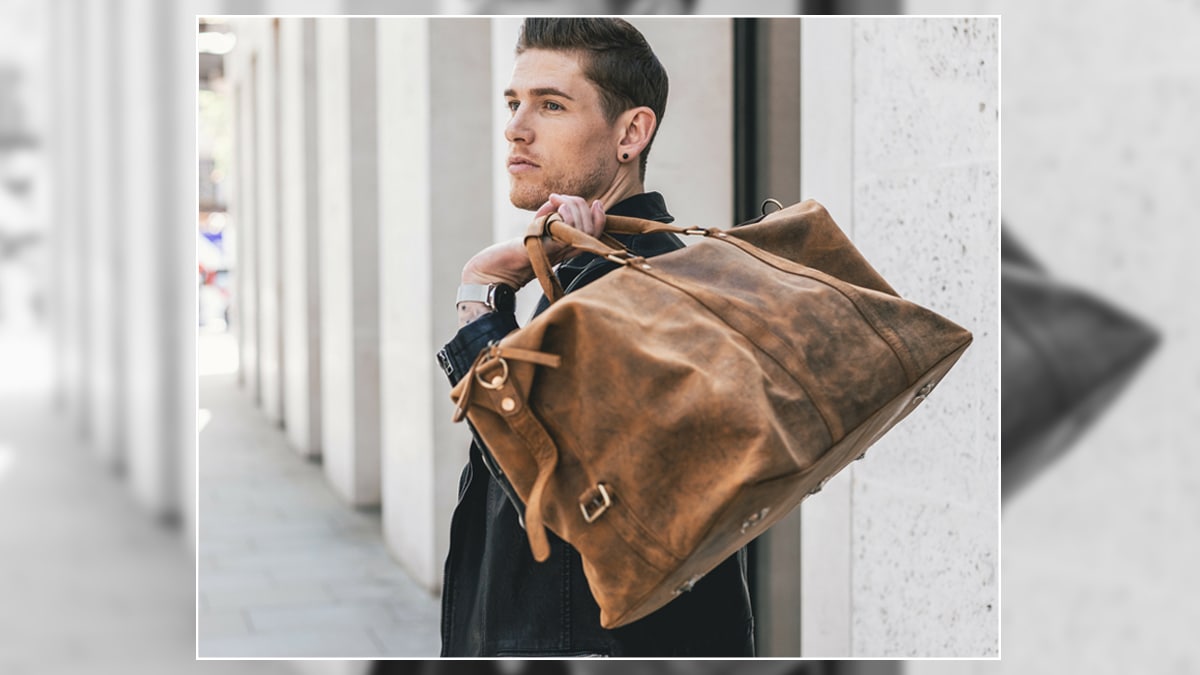 A man holding a duffle bag that is brown in color and it is one of the graduation gift ideas for nephews.