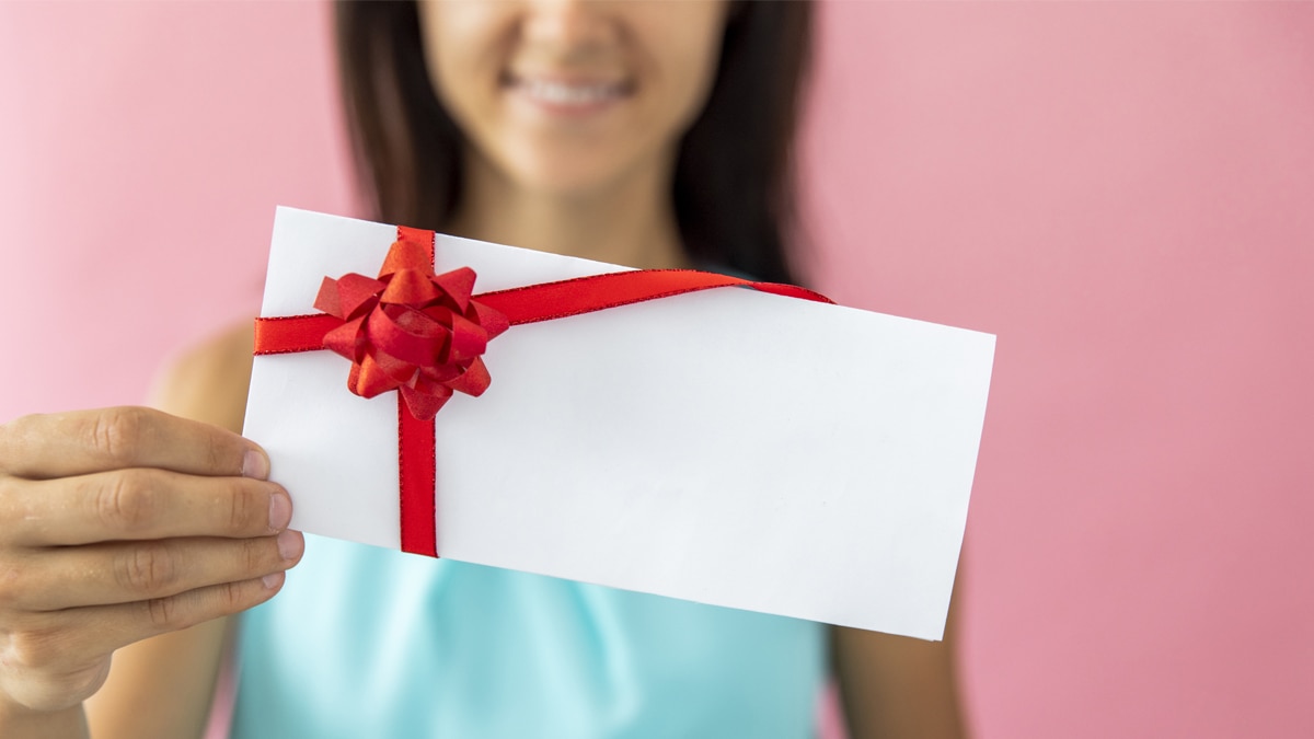 A girl smiling and holding a gift card with a red ribbon on it. A graduation gift ideas for sister.
