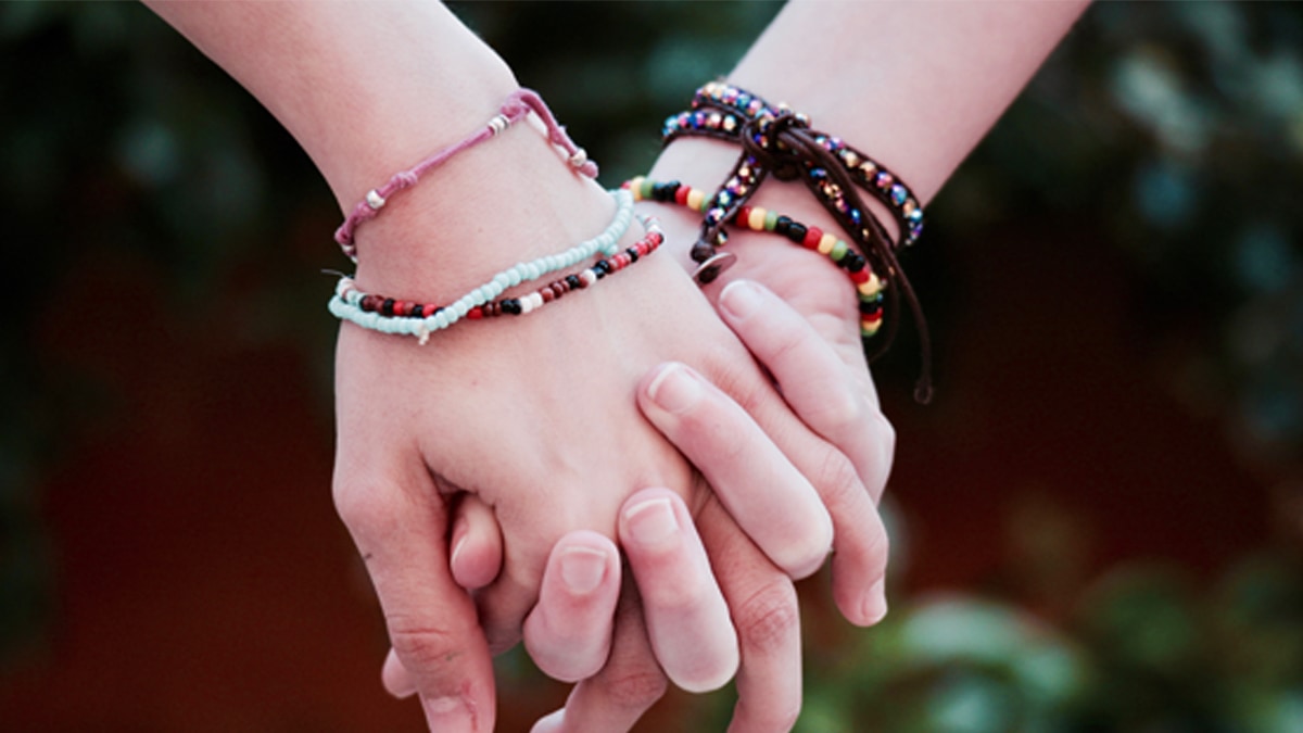Two friends hand in hand wearing friendship day bracelets