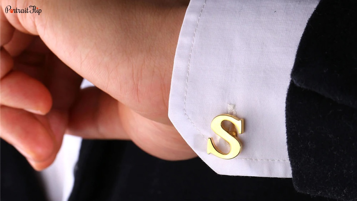 A mans sleeve with a cuff link with the initials of their partner on it.