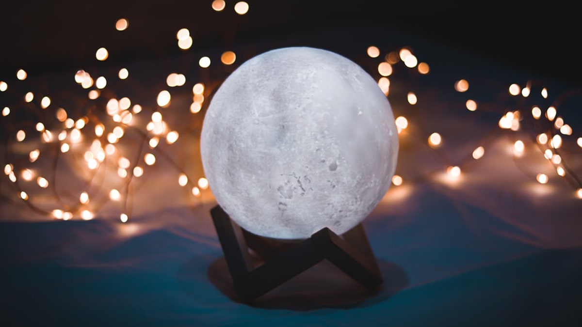 A customized moon lamp on a wooden stand surrounded with beautiful fairy lights