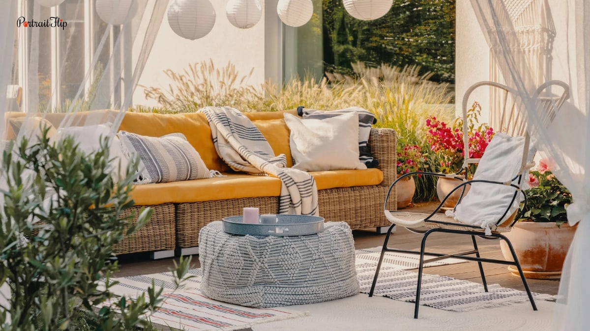 An elegant outdoor furnished area. There is a wooden cot with pillows and bedding that is yellow in color. There is a chair and a make shift table. The whole area looks very pleasing and relaxing. Outdoor trends in 2022.