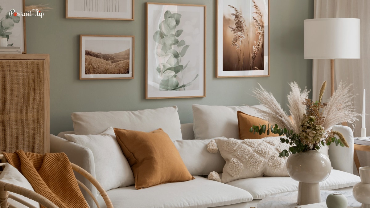 A living room with trends in home decor. There is a sofa, pillows on it and paintings on the wall. The whole living room is decorated in soft earthy tones.