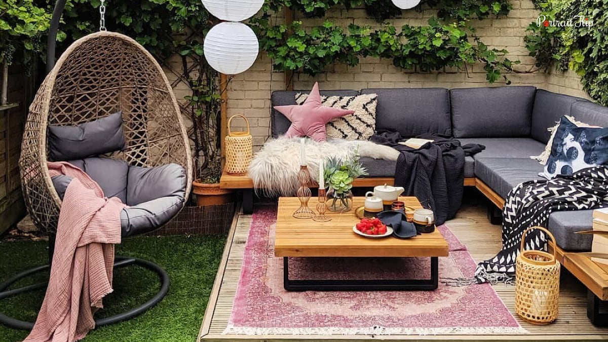 An egg chair that is sitting in an outdoor area. This patio trend of 2022 in home decor is comfortable and chic. There is a L-shaped couch with pillows and blankets. This is a home decor trend.
