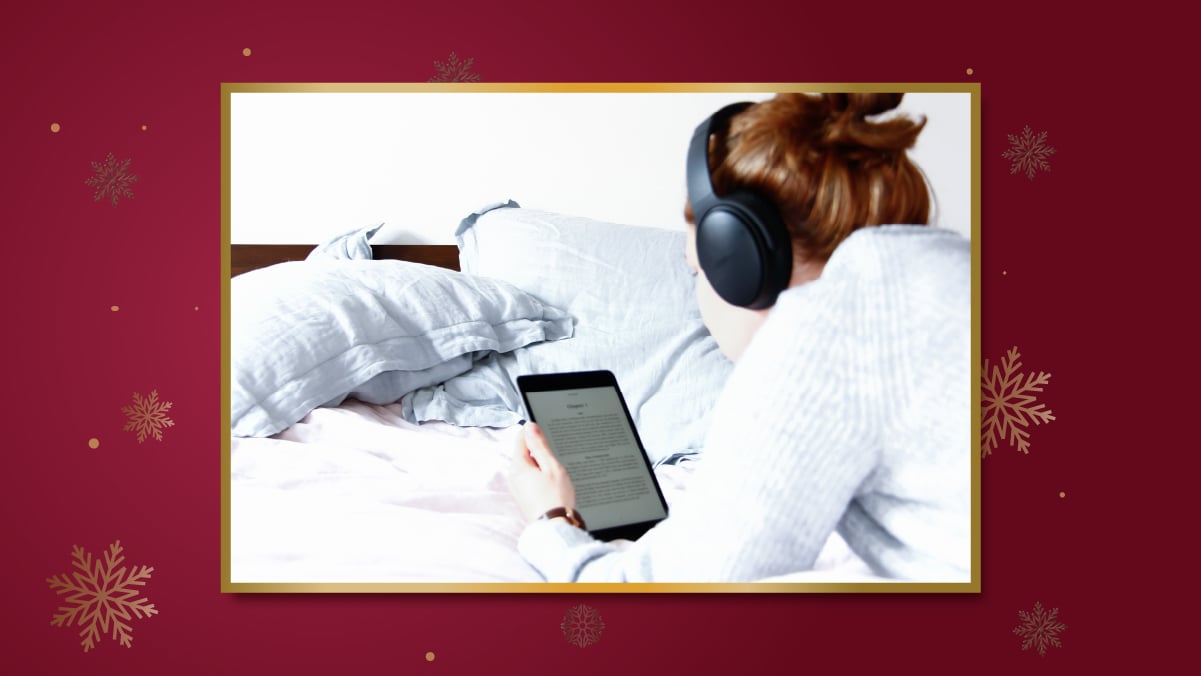 a girl in lying front in her bed reading a book on Kindle