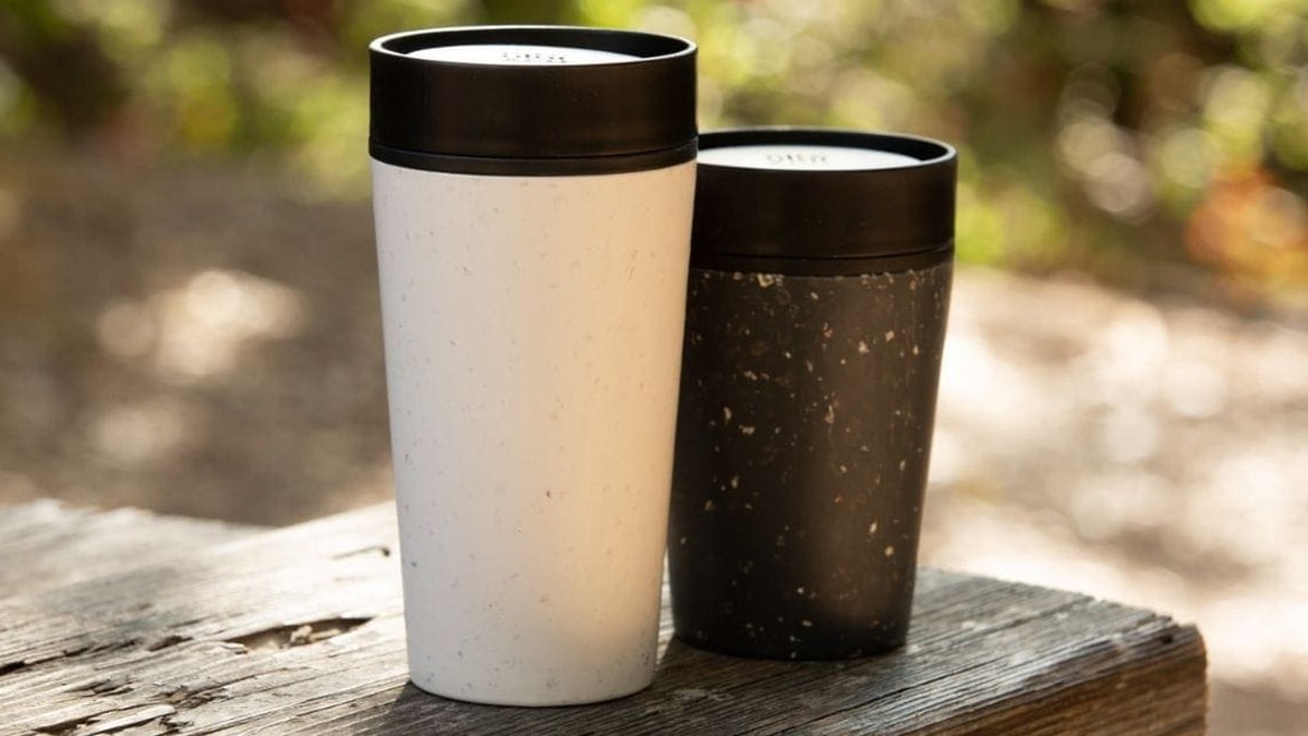 two reusable coffee mugs on a wooden bench