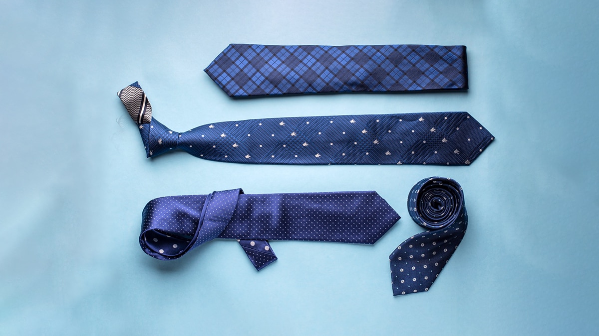 3 silk ties opened and 1 tie rolled on a blue surface. 