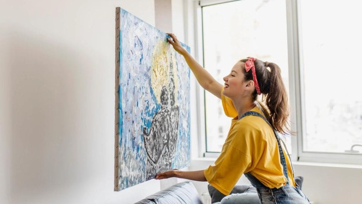 a woman hanging an oil painting at a suitable spot in her home to avoid it from getting dirty