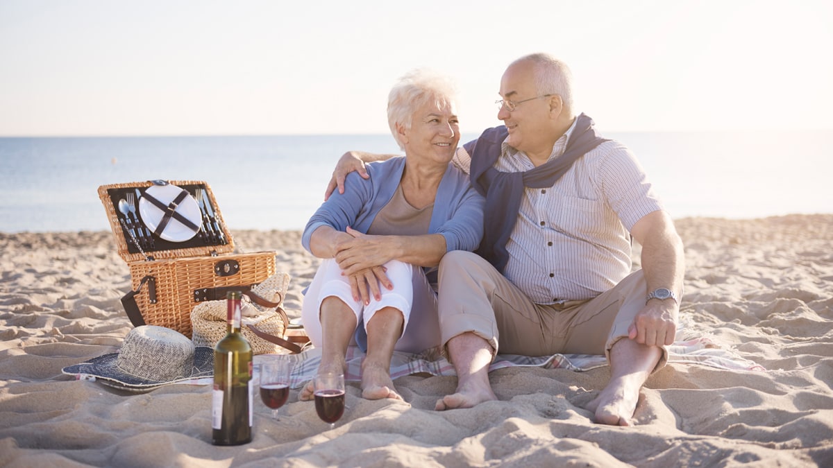 an old couple sitting on the beach looking at each other in an romantic way 