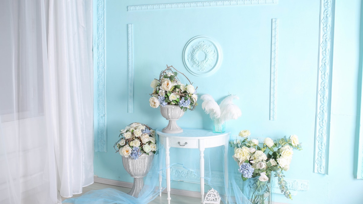 An antique wall paneling design in teel blue color. A white table with flower vases placed on it.