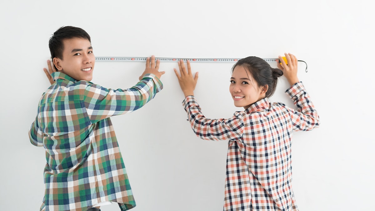 a girl and a boy measuring the length of the wall with a measuring tape