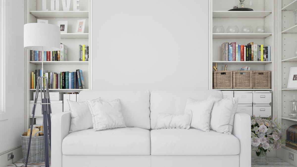 A living room set up that has two white shelves on both the corners of the couch with a white couch placed right in the center of the room.
