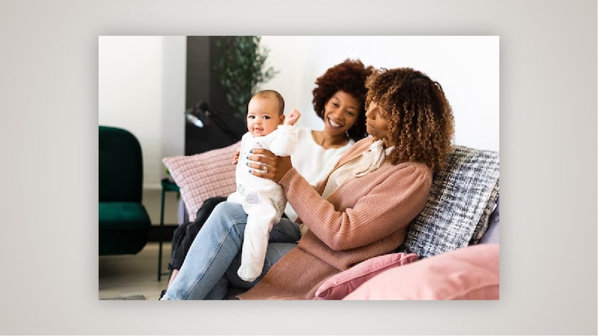 Two woman laughing while one is playing with a baby