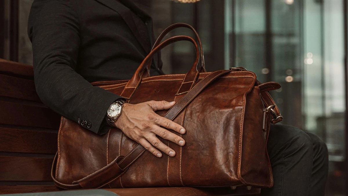 A man holding a custom travel leather bag in deep dark brown color 