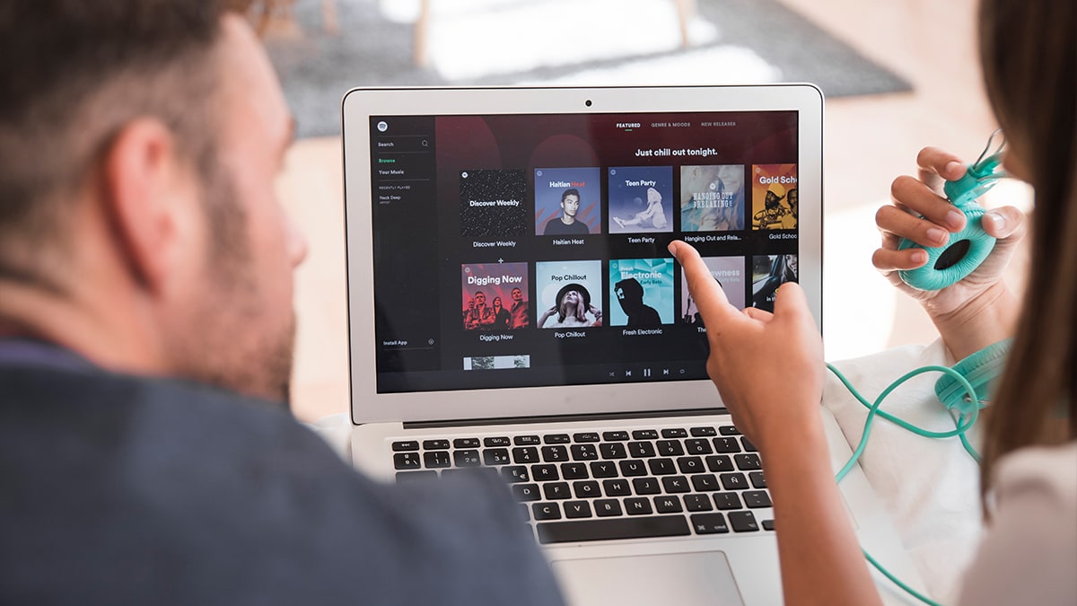 Pointing finger towards laptop screen that shows Spotify playlist