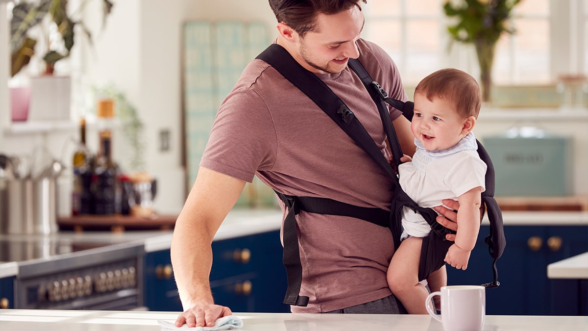A man holding a baby in a baby carrier while cleaning the table as a gift for valentine's day