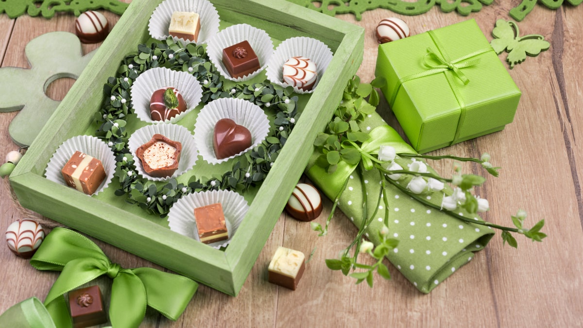 A box of chocolate covered in green box with green gift, cloth, and floral stems as a gifts for St. Patrick's Day