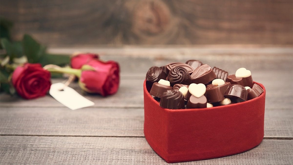 Chocolate in a red heart shaped box with a blur image of rose behind it place on a wooden table