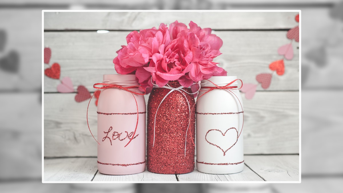 Mason jars decorated with sparkling glitter with a artificial flower added to it on a wooden table