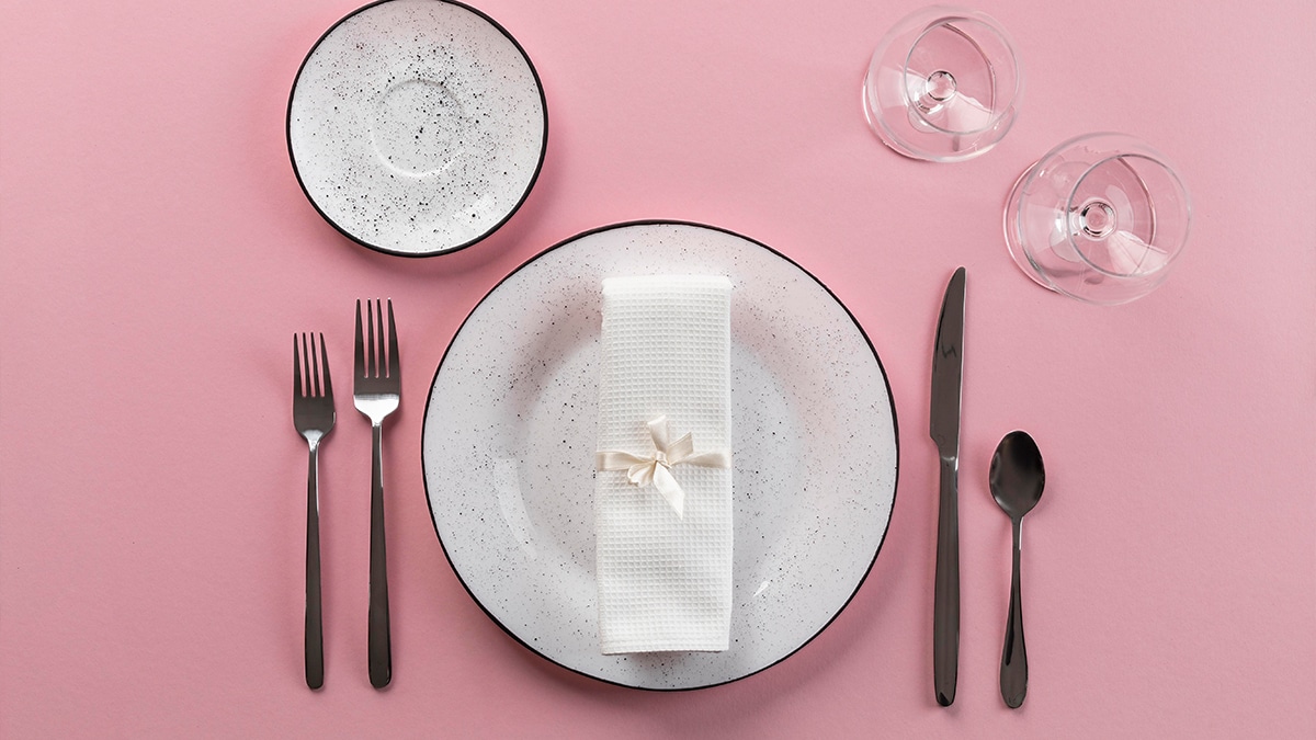 Plates, with fork, spoon and butter knife beside it with two glasses in a pink background 