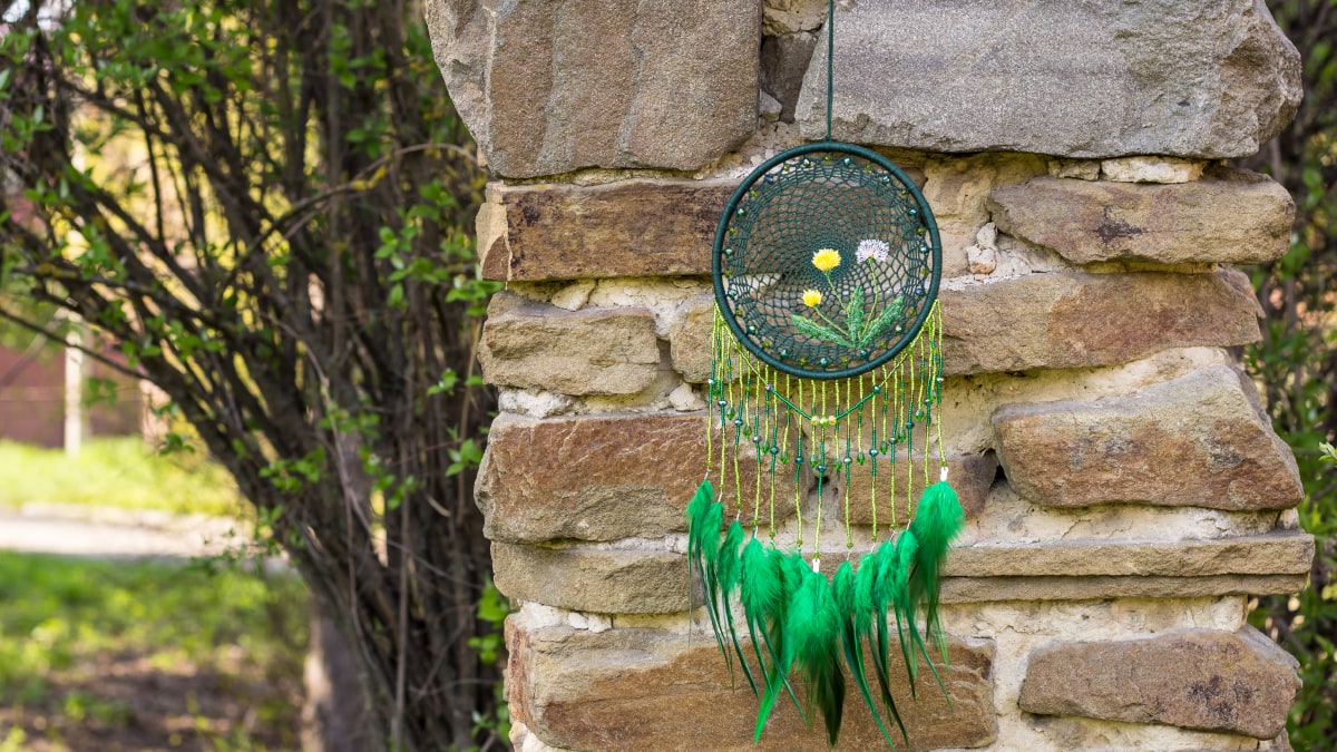 A dreamcatcher hanging in front a brick wall with stems like tree in the background