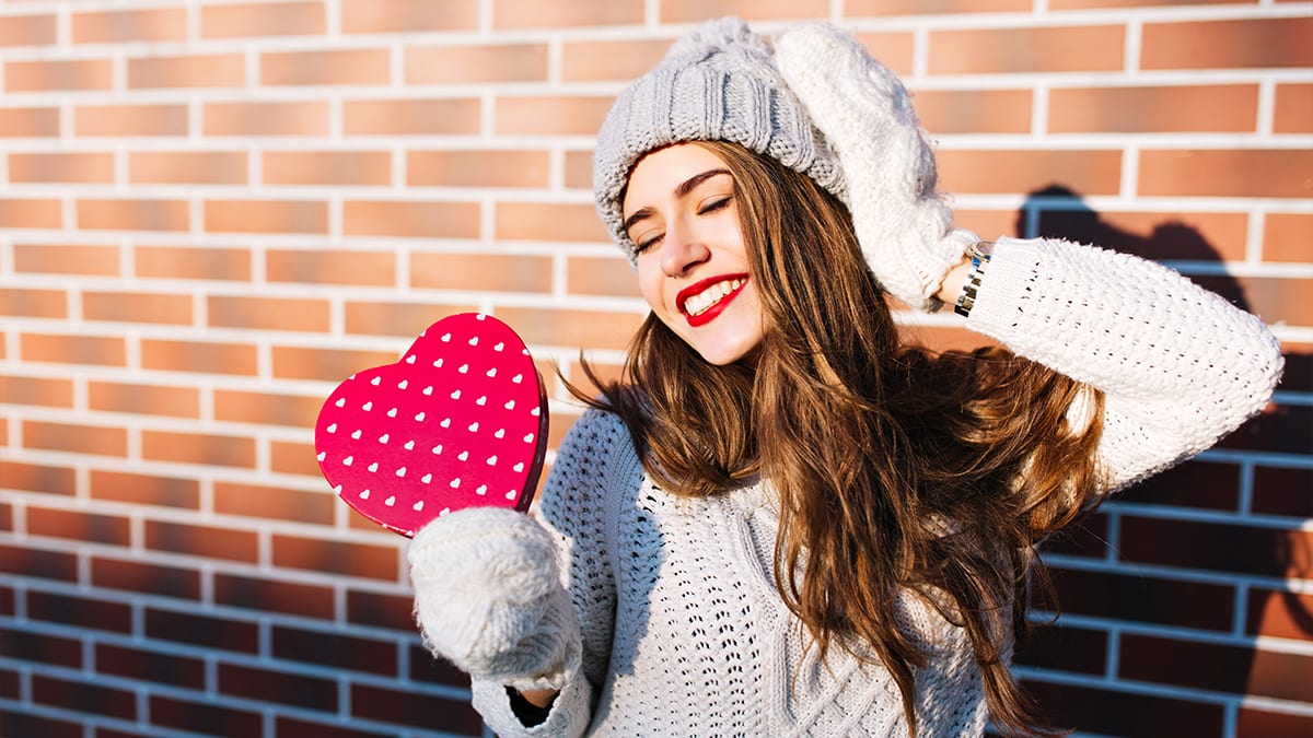 A woman posing with a heart shape box with white gloves
