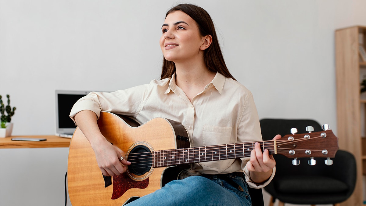 Woman playing guitar while sitting in a living room and smiling 