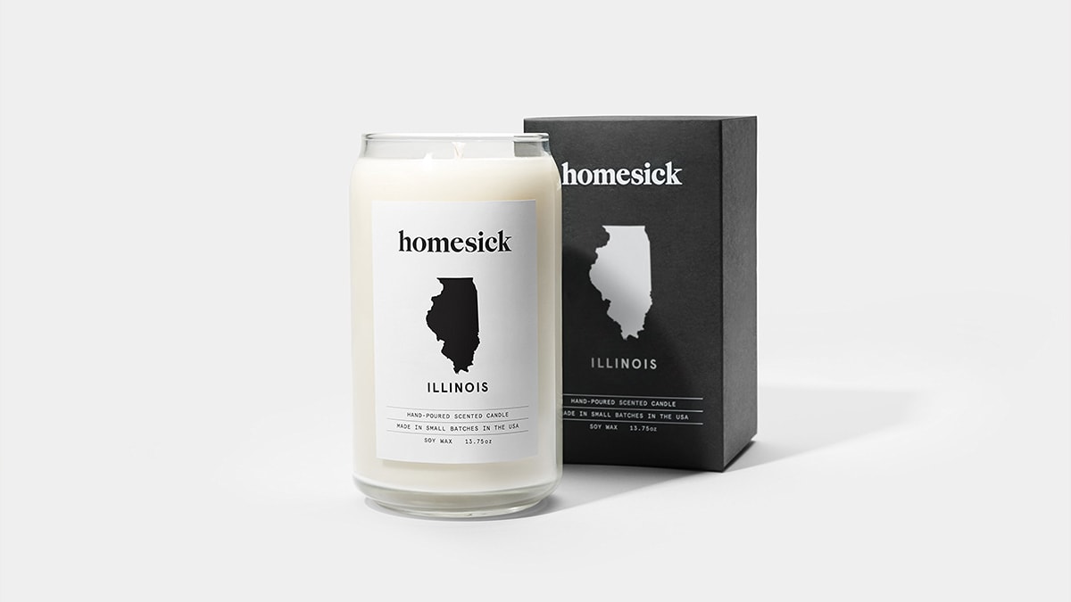 Homesick candles with its cover behind it.