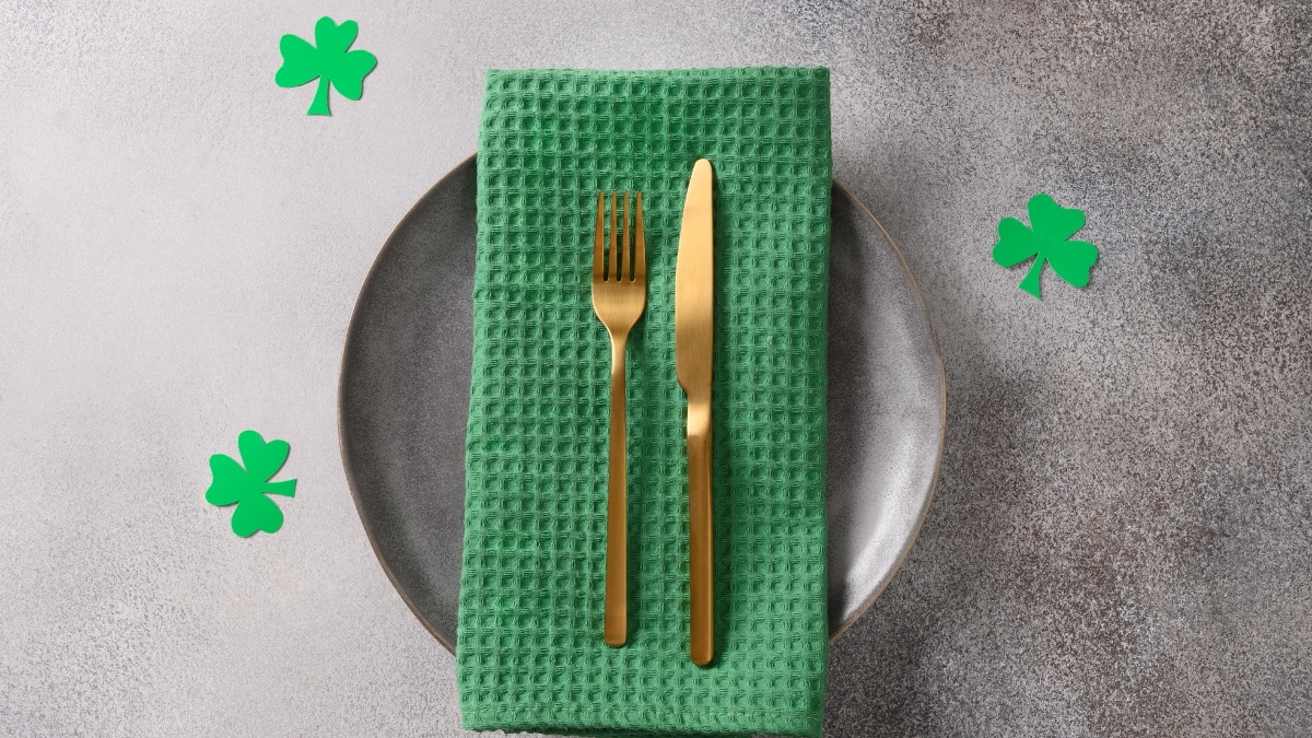 Green kitchen table cloth with gold plated fork and butter knife on a cemented type plate