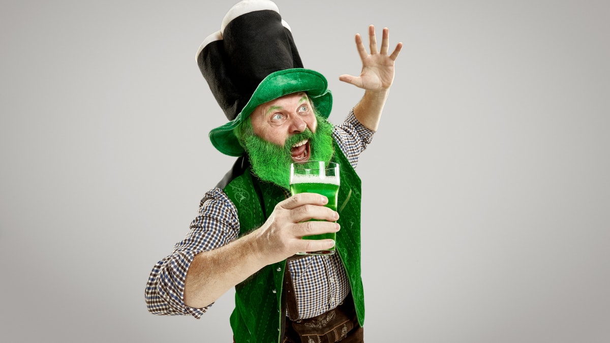 A man wearing St. Patrick's Day costume with green beard, drink, and hat