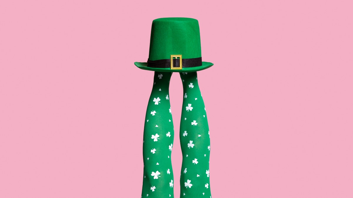 Legs wearing a pair of green long socks with clover leaf print with a hat on top 