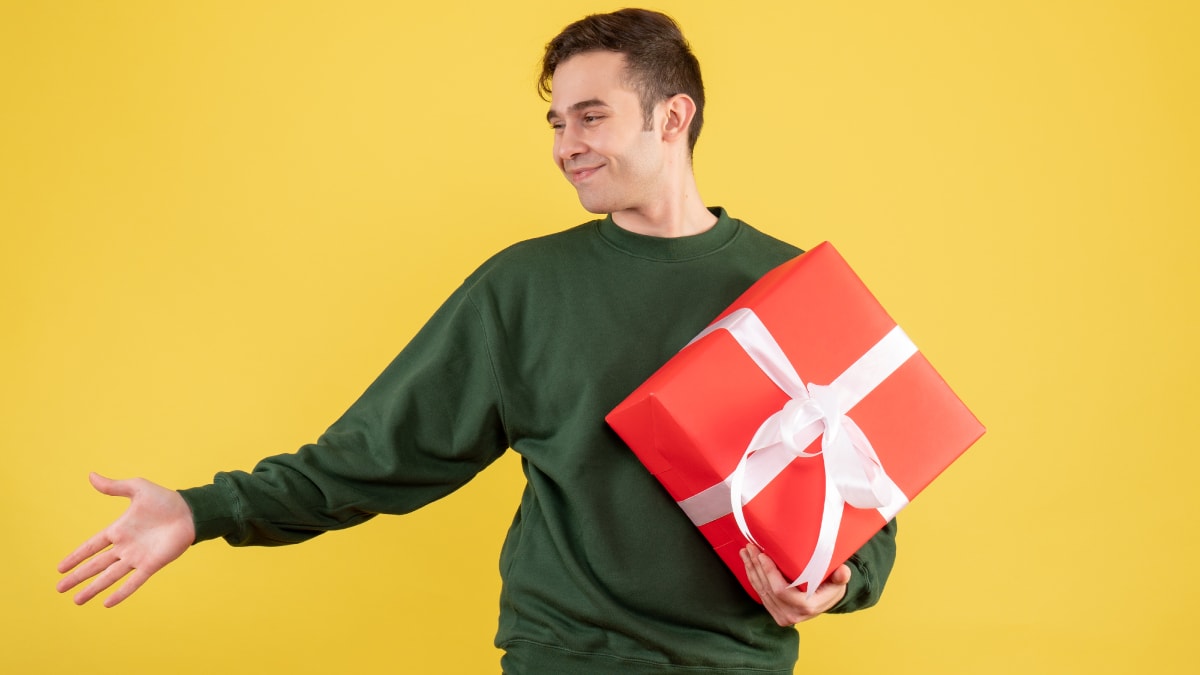 A man wearing dark green sweatshirts holding a red wrapped gift in a yellow background