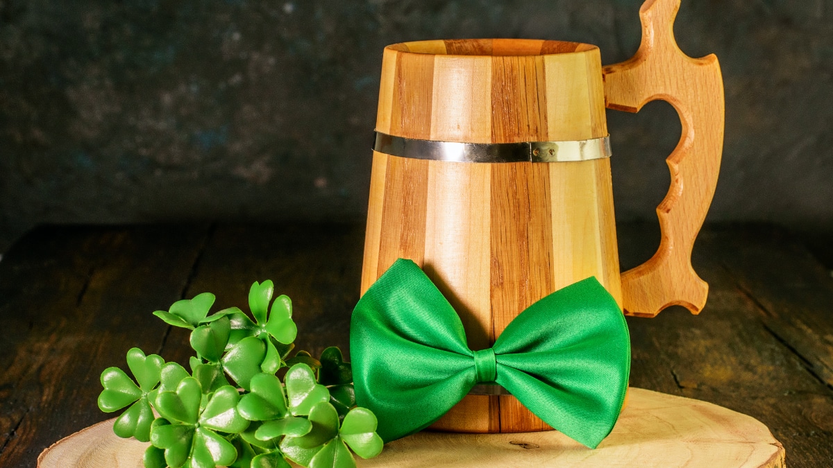 A wooden mug with green bow and clover leaf placed on a wooden cut design table 