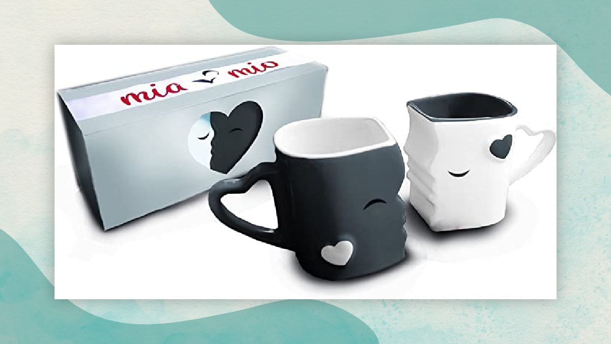 A pair of black and white colored cups with a kissing gesture, having hearts imprinted and a heart shaped handle in a white background. 