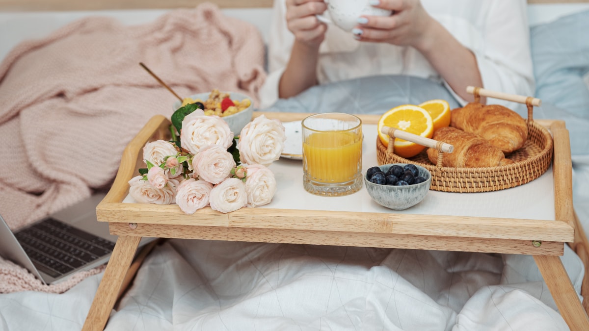 A table bed that serves croissant, juice and white roses depicting breakfast in bed
