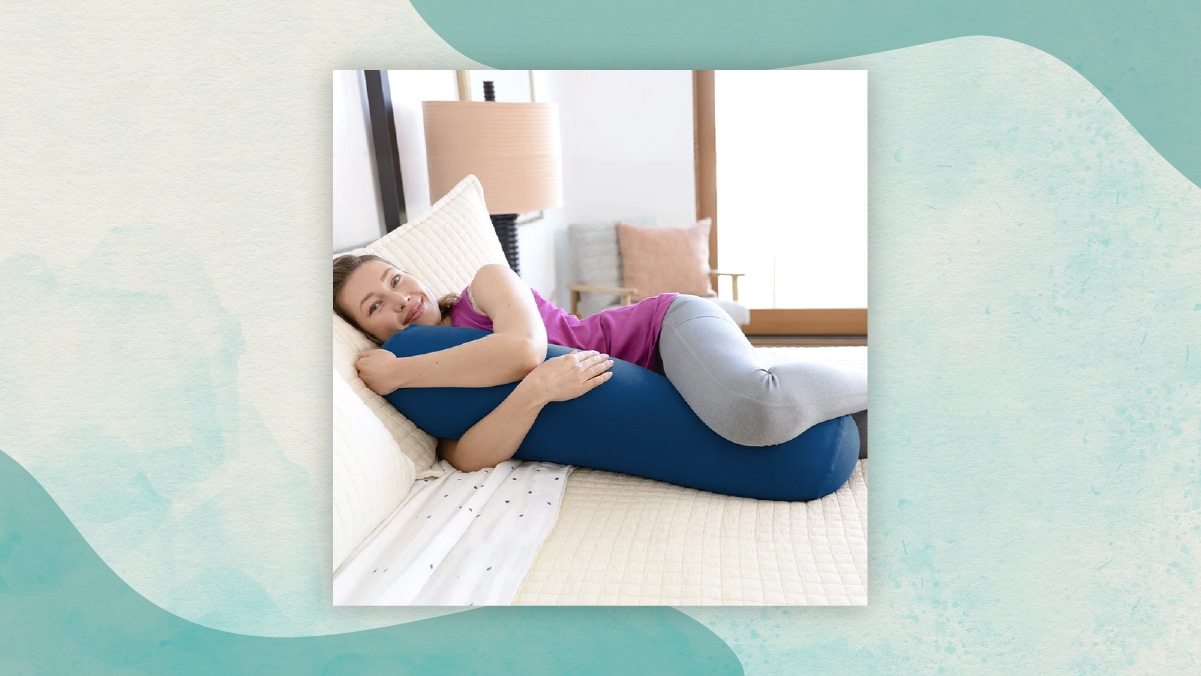 A women laying on the bed holding to a blue color pillow with a pink lamp and  pink coushion in background. 