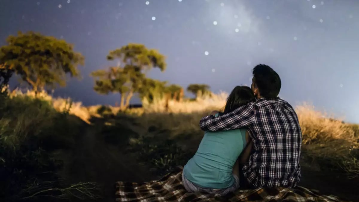 Back view of couple stargazing while holding each other