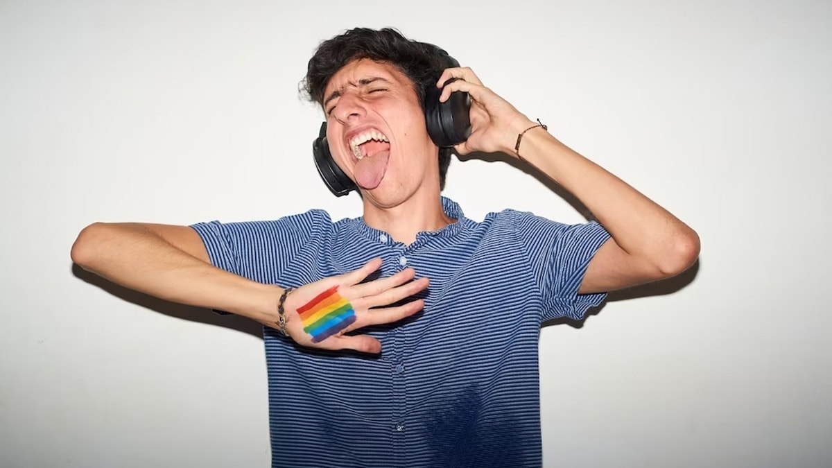 A man wearing headphones with showing the pride rainbow symbol marked on his palm.